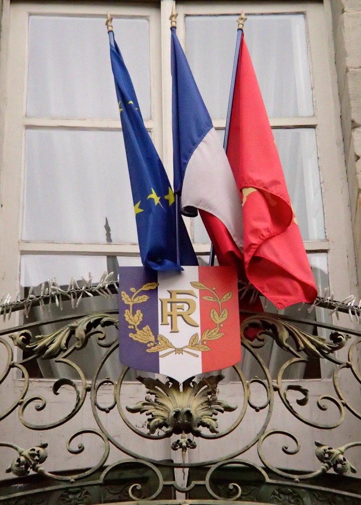 The flags of the European Union, France, and the Languedoc-Roussillon region above the entrance to Hôtel de Rolland, an 18th century hôtel particulier which is now the Mairie (town Hall)  on Rue Aimé Ramond.