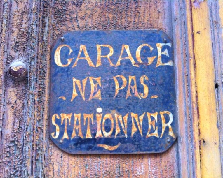 Antique "No Parking" sign on a garage along Rue Jean Bringer.